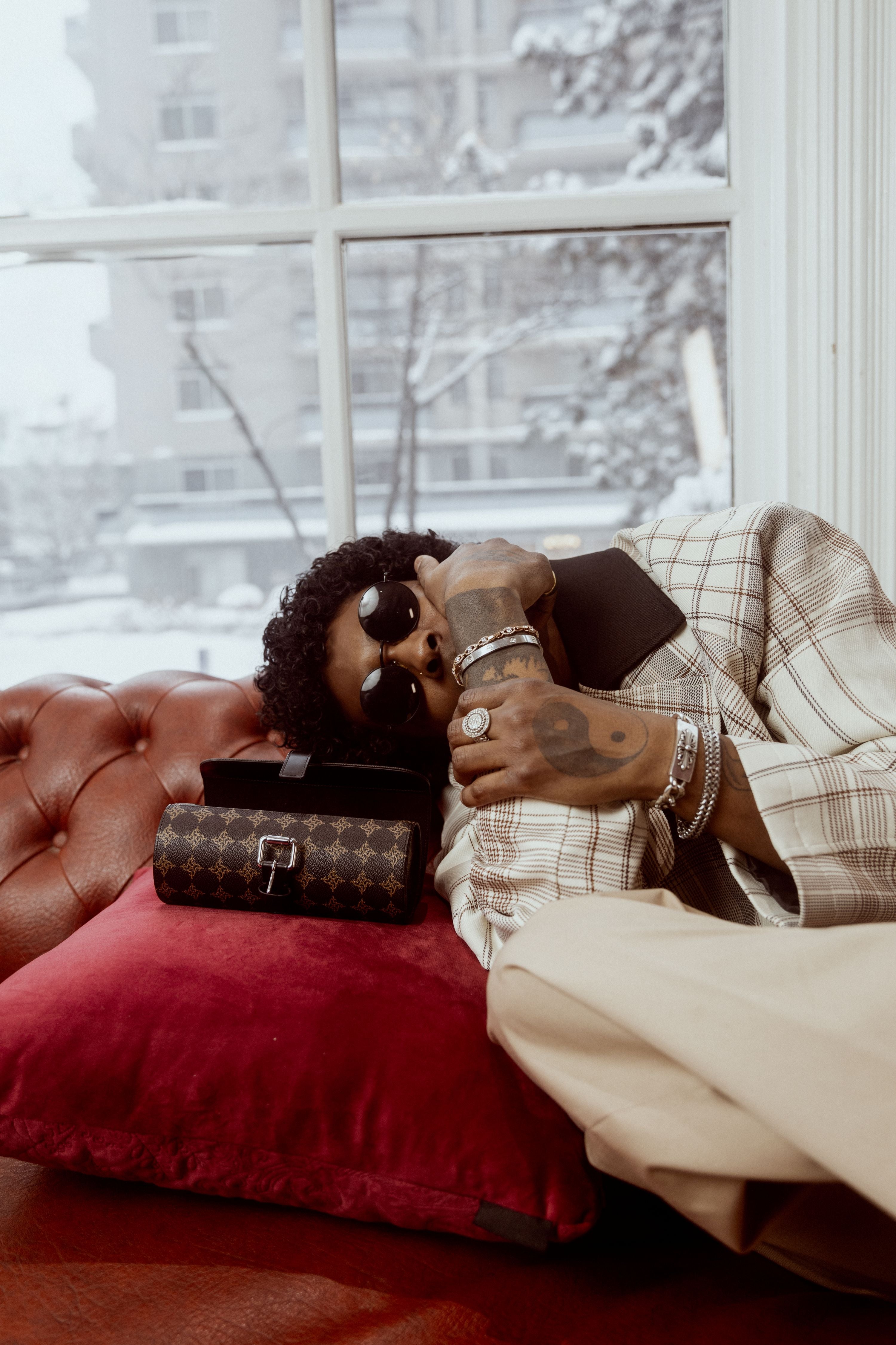 A person sitting on a couch holding a watch case with a snowy outdoor view through the window.